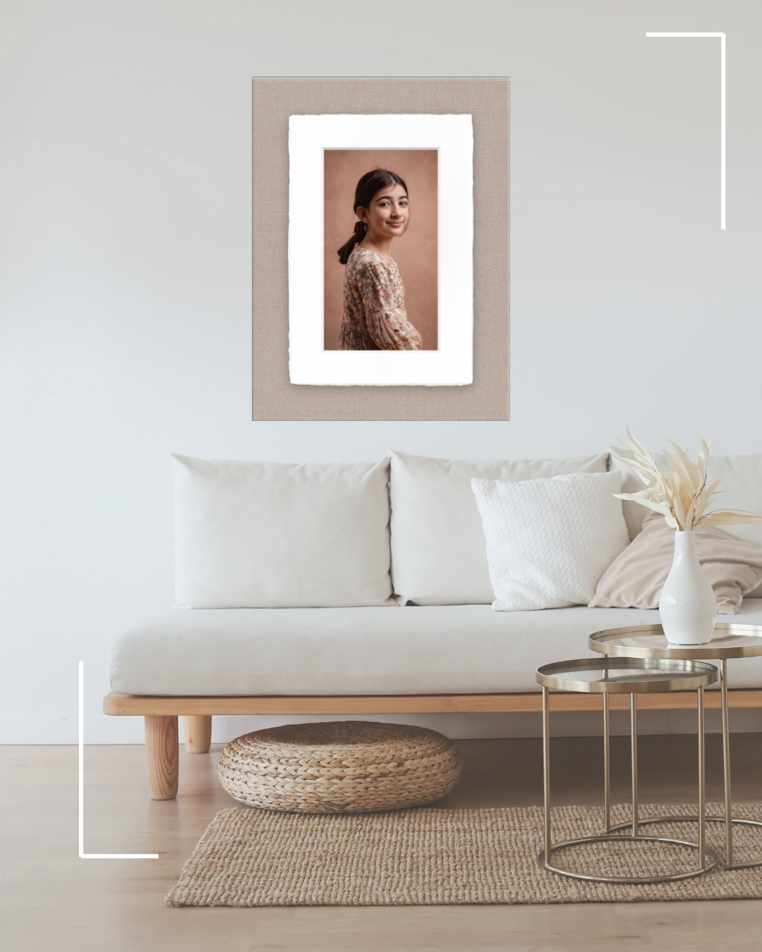 Modern minimalist living room with white sofa, round side tables, woven pouf and framed portrait on beige wall.