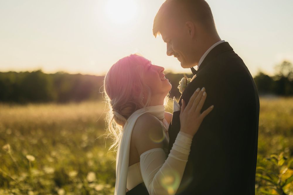 A romantic couple embraces in a sunlit field during golden hour as sunlight creates a dreamy backlit glow.