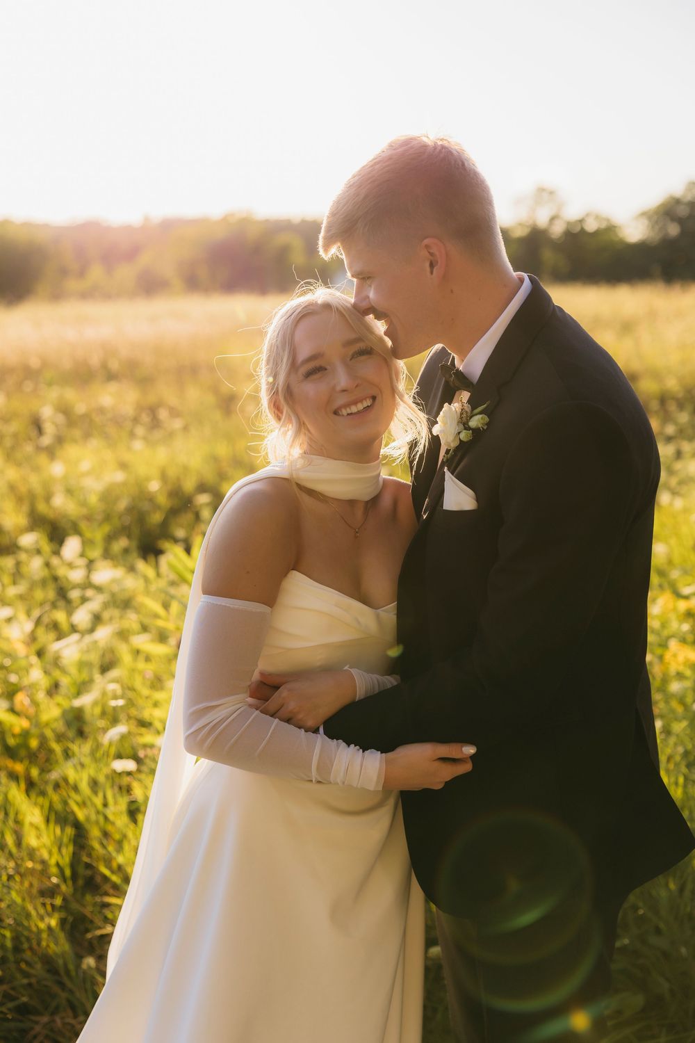 A couple shares intimate moments in a sunlit field of wildflowers during a romantic wedding photoshoot.