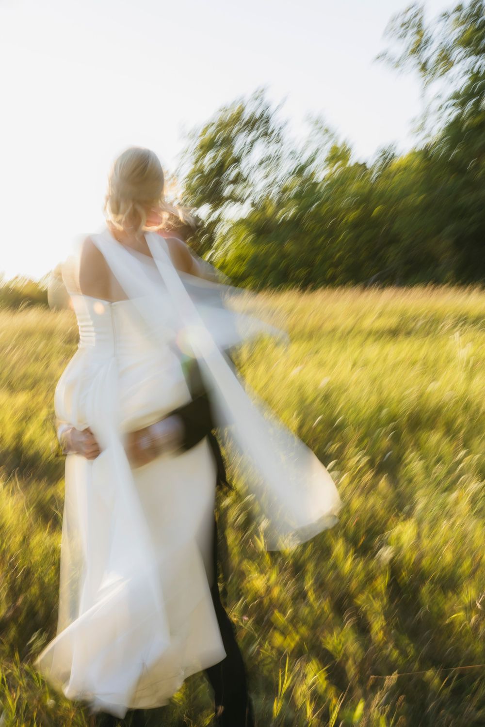Dreamy motion-blur wedding photos show a couple dancing and twirling in a sunlit meadow.