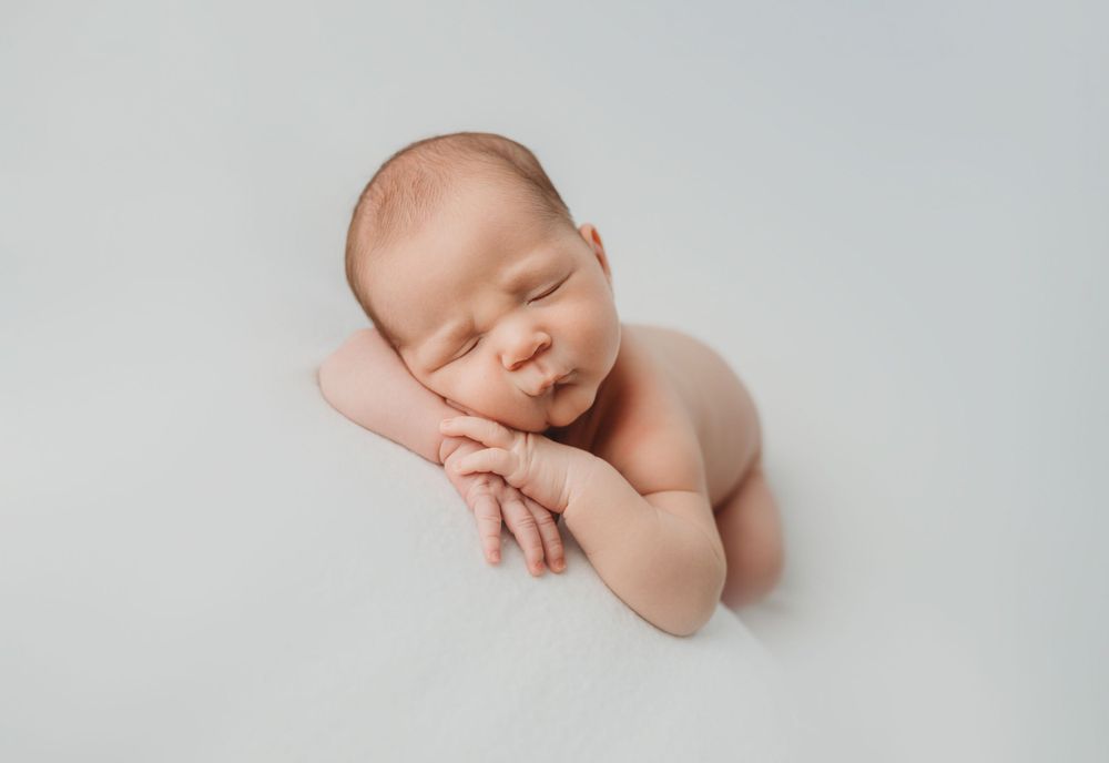 Minimalist portrait of sleeping newborn with hands curled on white background.