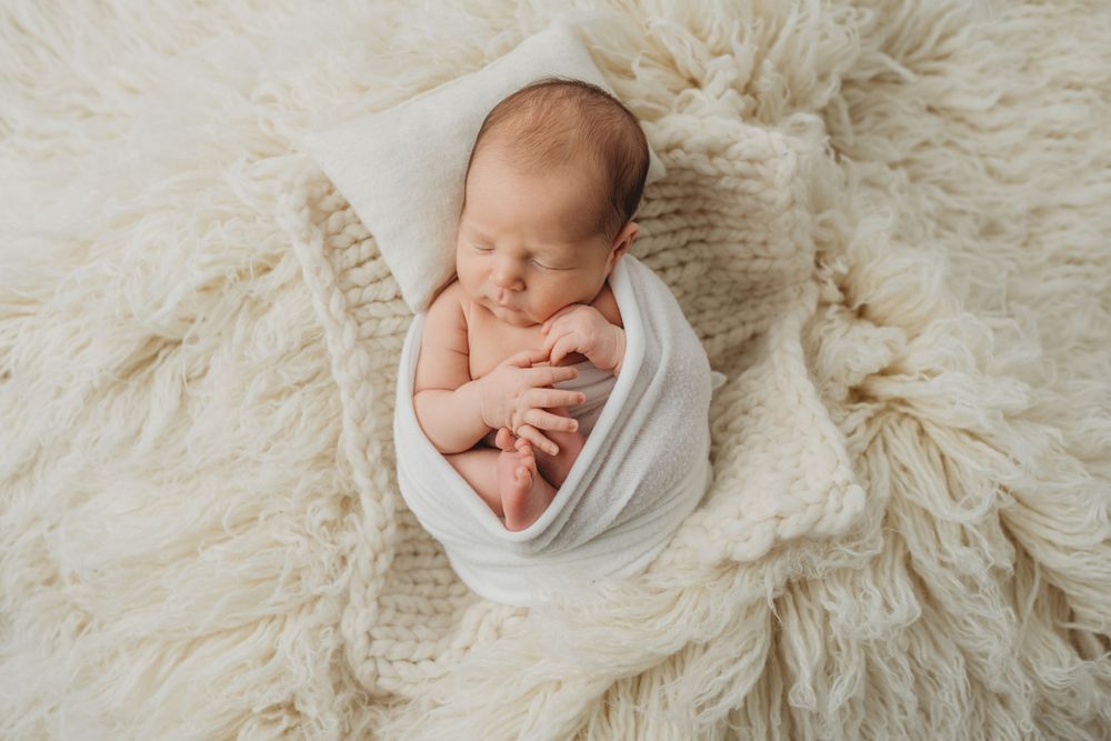 Peaceful sleeping newborn wrapped in white swaddle on textured cream blanket.