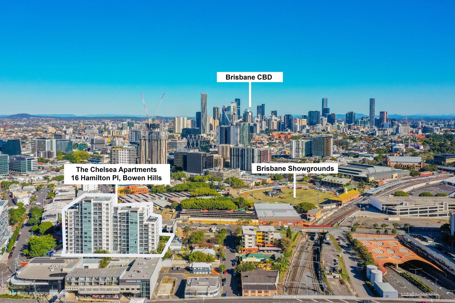 Aerial view of Bowen Hills with The Chelsea Apartments, Brisbane CBD skyline, and Showgrounds visible.