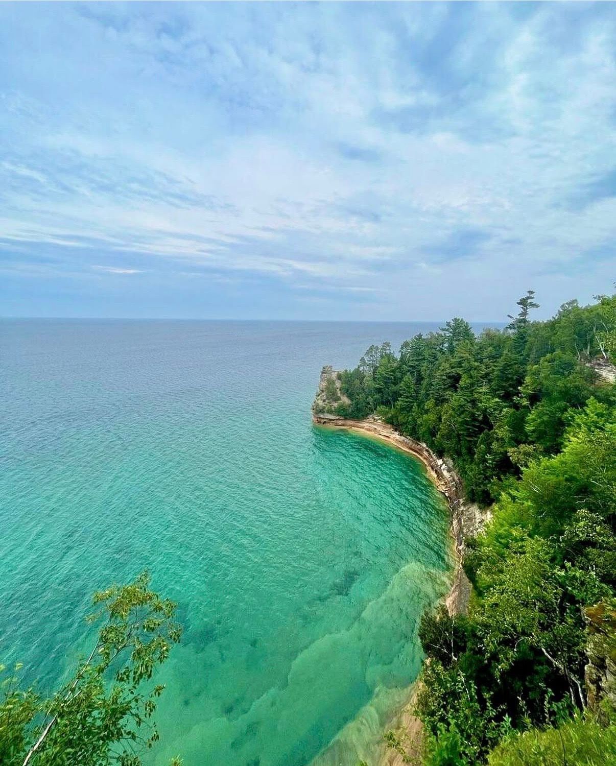 Turquoise waters meet steep cliffs covered in lush green forest along the scenic Pictured Rocks shoreline along Lake Superior in Michigan.