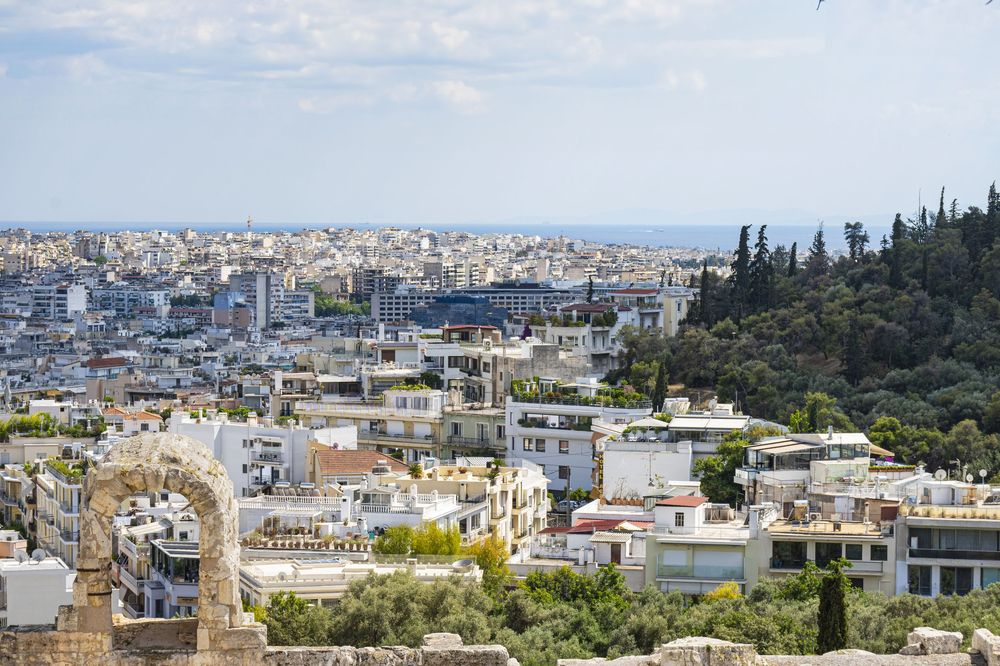 Panoramic cityscape view of Athens Greece showing dense urban buildings with ancient ruins and mountains in the distance.