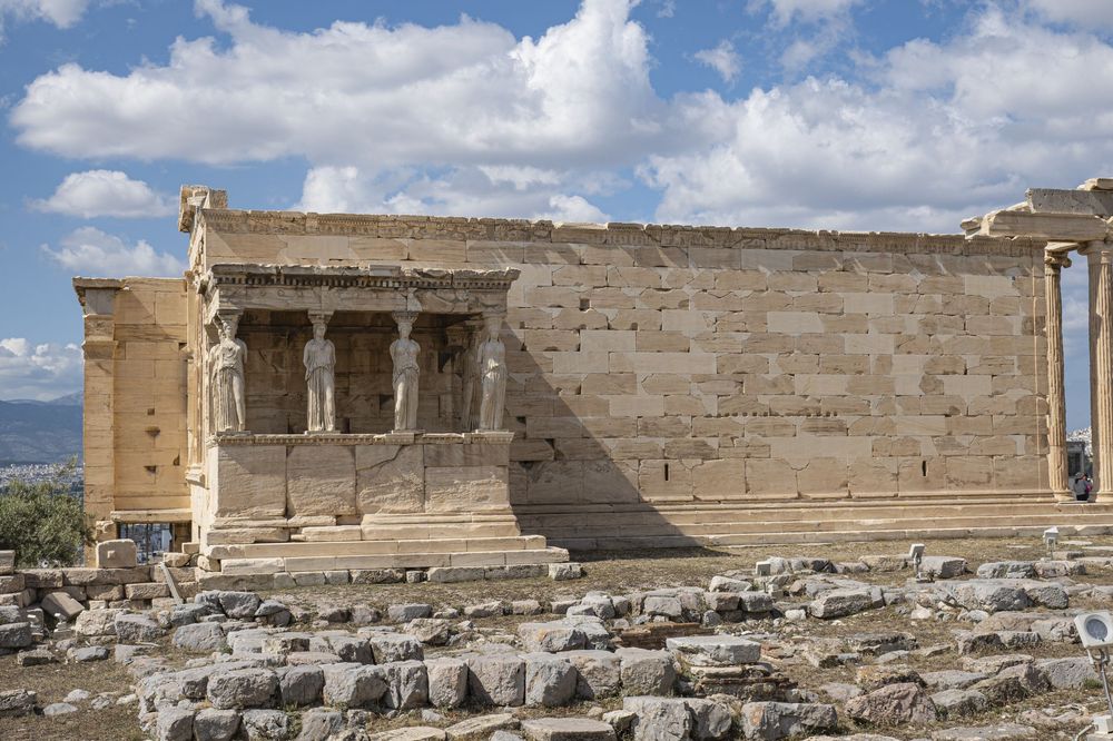 Ancient stone ruins and columns of a historic archaeological site under blue sky with scattered clouds.