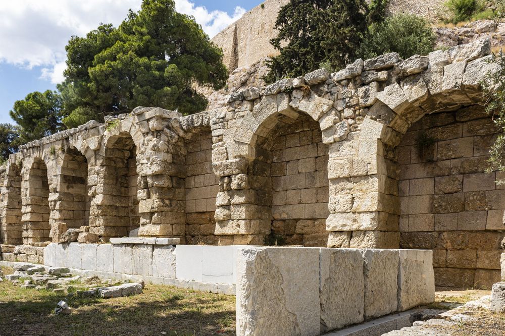 Ancient stone ruins and arches line a path along a mountainside in a historic archaeological site.