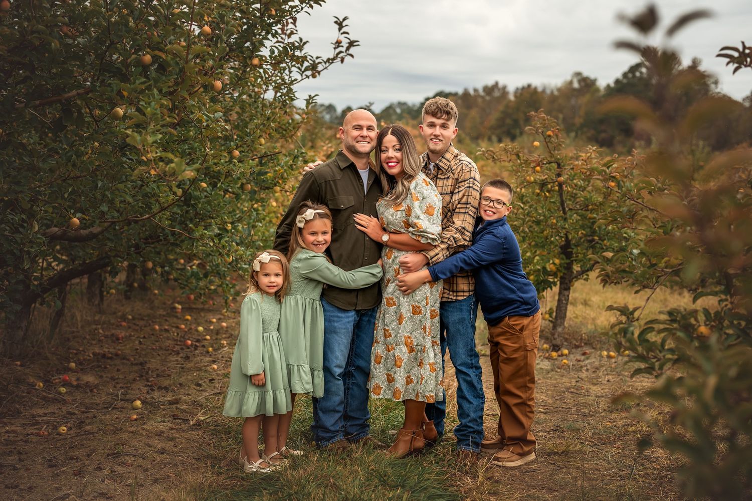 A group in coordinated autumn outfits poses together in a rustic outdoor setting during golden hour.