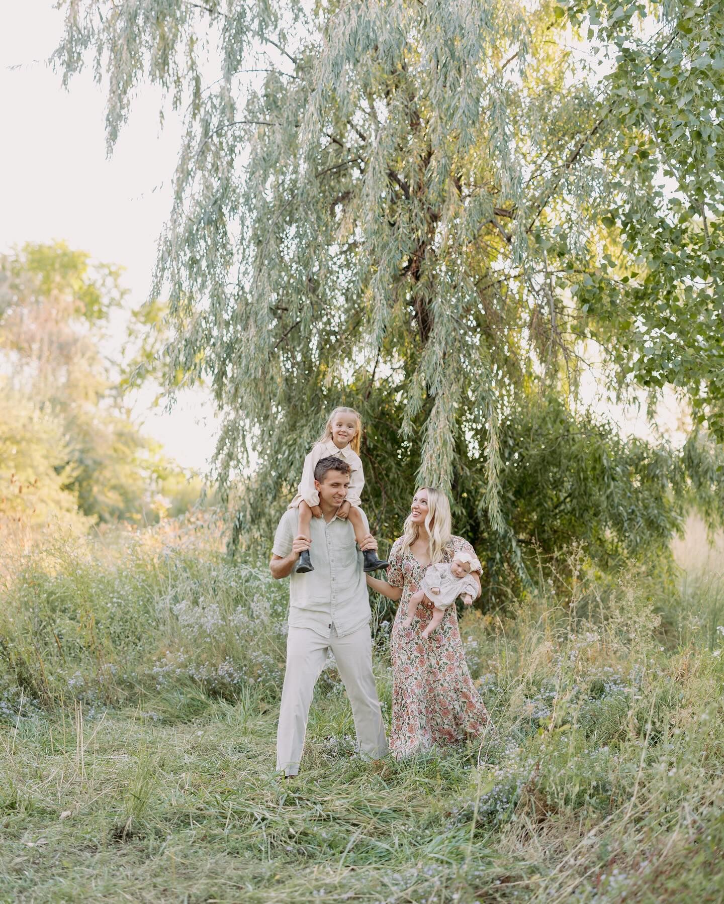 A playful family photoshoot captures candid moments under weeping willow trees in a natural setting.