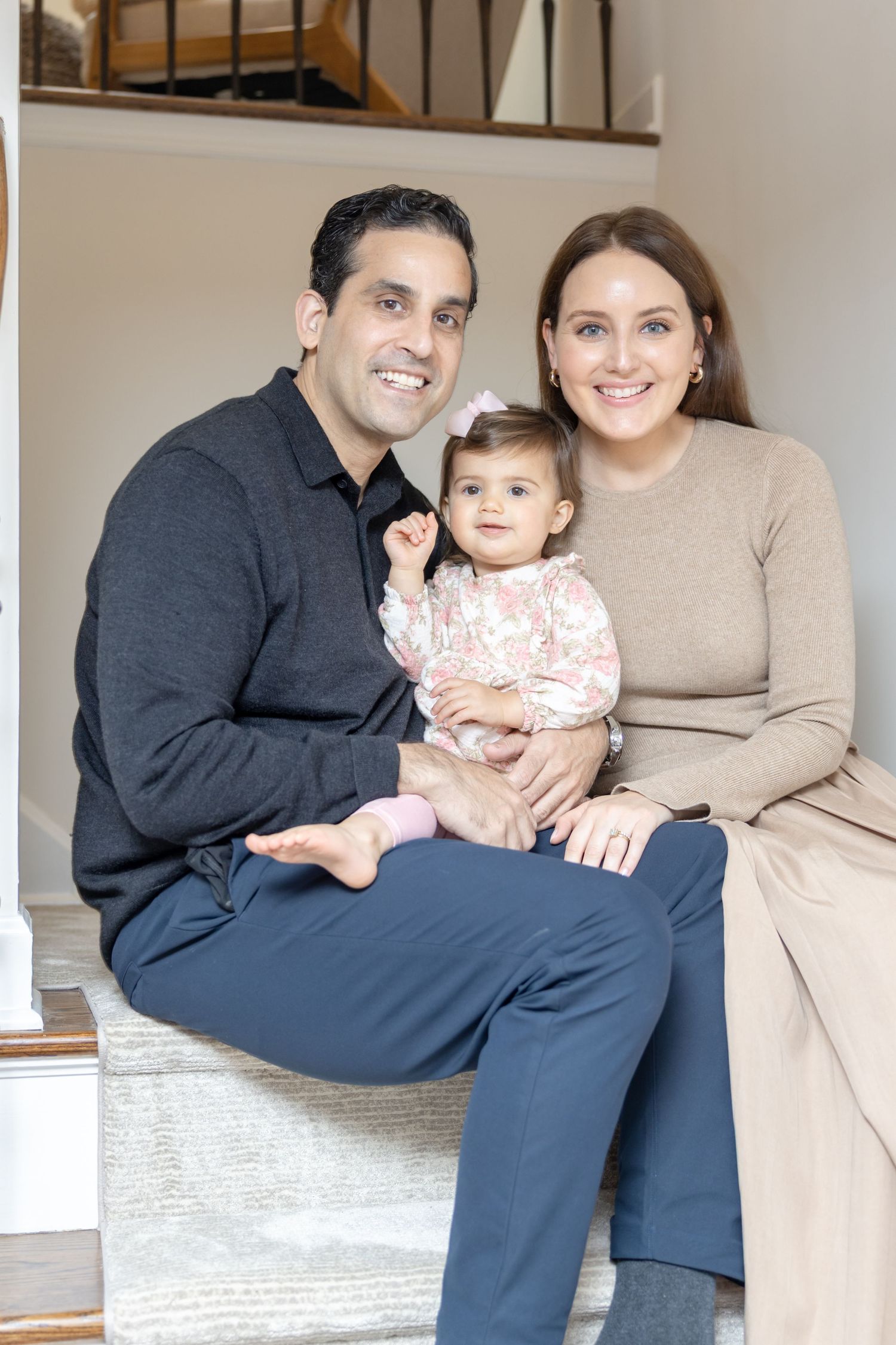 Family sitting together on beige couch in living room during casual indoor photo session.