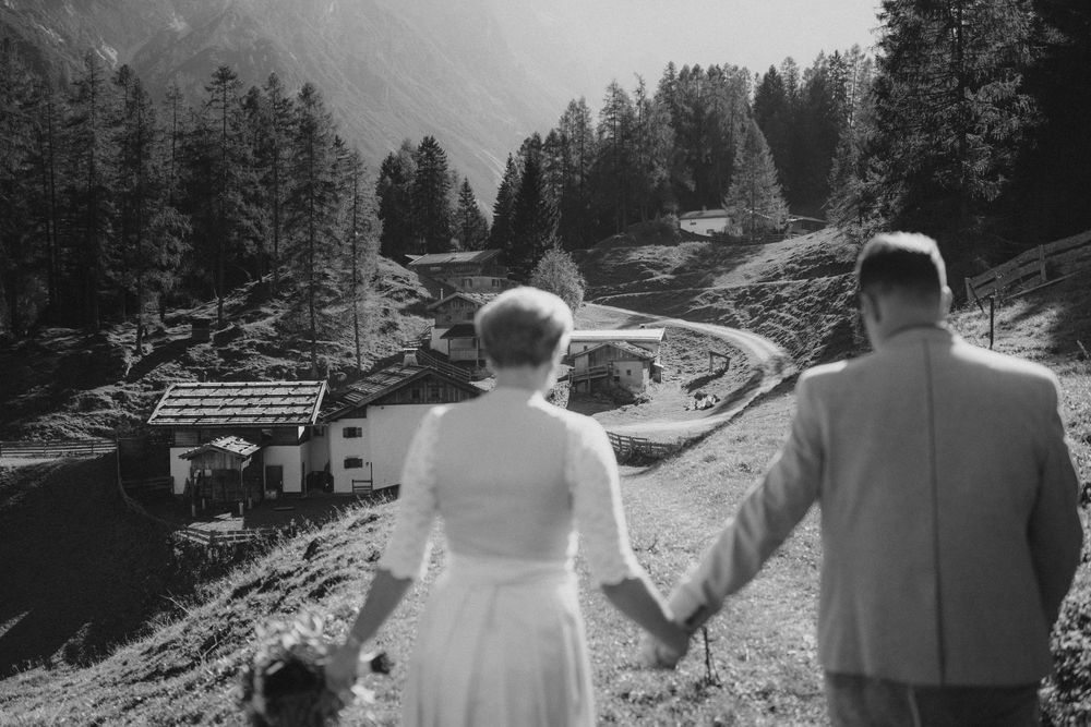 Schwarz-Weiß-Aufnahme: Brautpaar blickt Hand in Hand auf die Bergbauernhöfe im Stubaital, Tirol