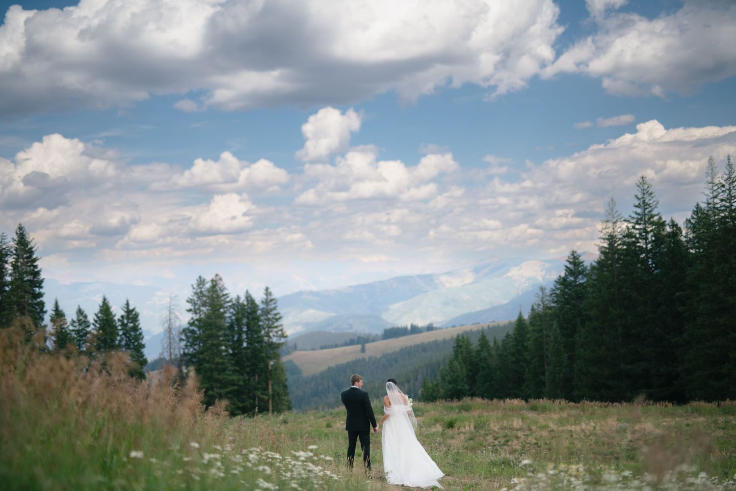 A scenic mountain wedding ceremony under bright blue skies and puffy clouds.