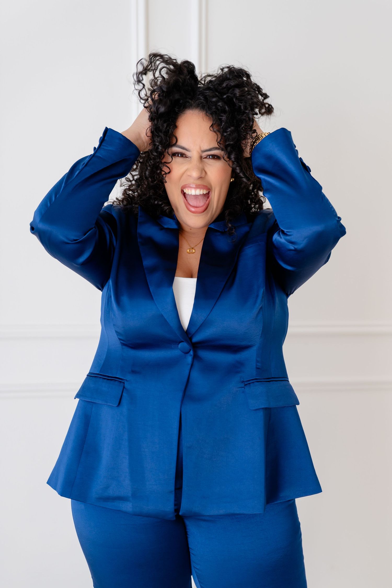 A person in a navy blue suit throws money bills in the air while dancing and celebrating in a white room.
