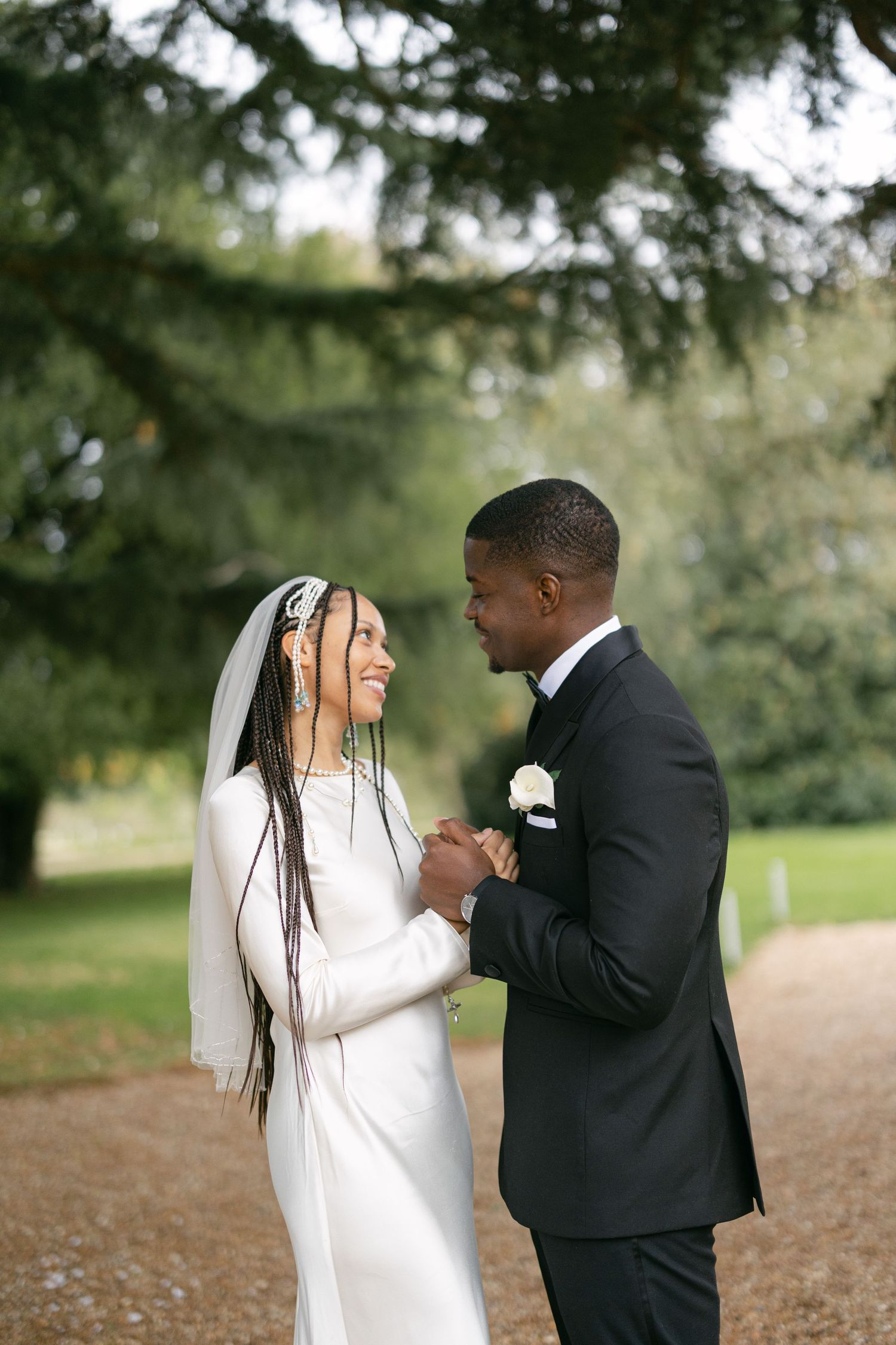 Elegant couple poses in formal wedding attire between classic stone columns, with bride holding blush pink bouquet.