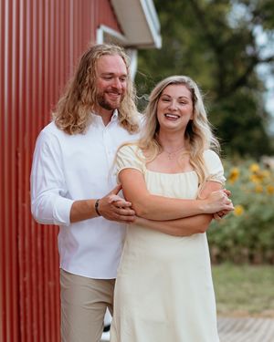 Playful couple photos against a red barn wall showing natural candid and documentary moments. A couples photographer in Central Michigan