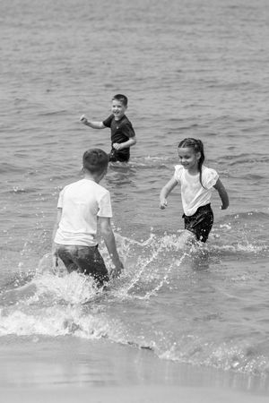 Children playing and splashing in the water at the beach captured in black and white. Beach sessions. Beach photographer.