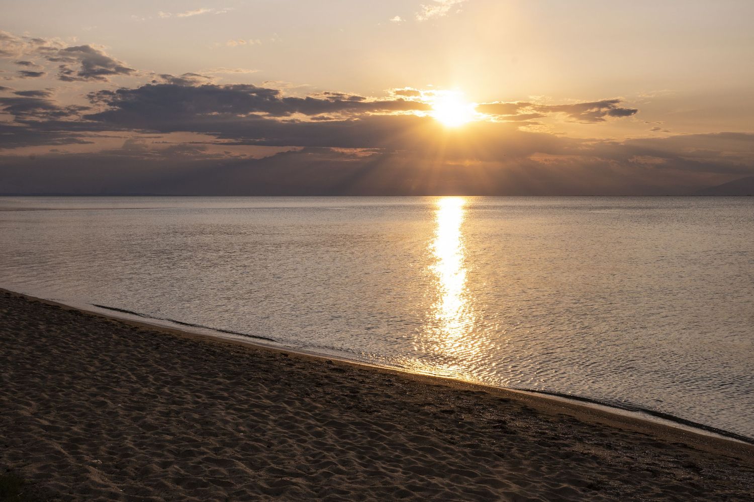 A stunning sunset over the ocean creates a golden path of light reflecting on the calm water's surface.