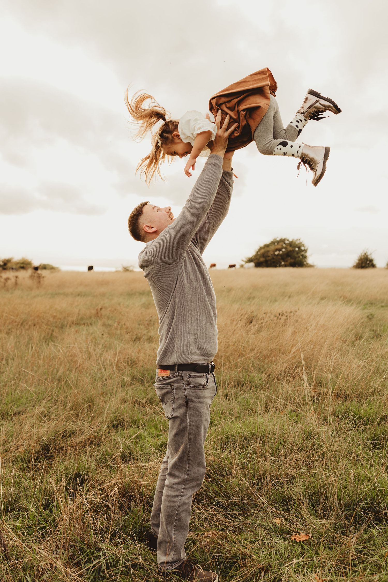A sequence of five photos showing a playful moment between parent and child in a golden grassy field at sunset.