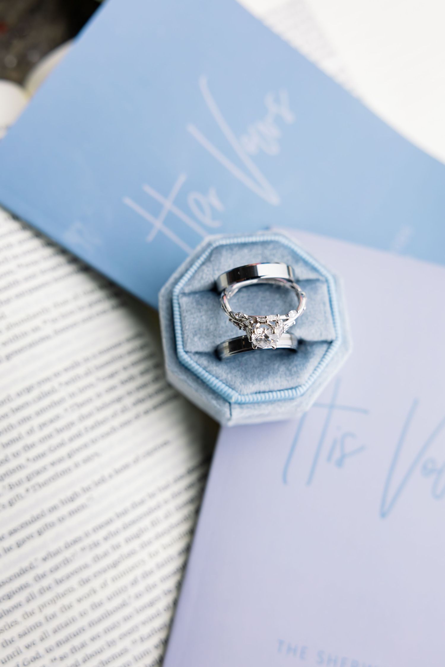 A delicate engagement ring with diamonds sits in a light blue velvet hexagonal ring box on white paper.