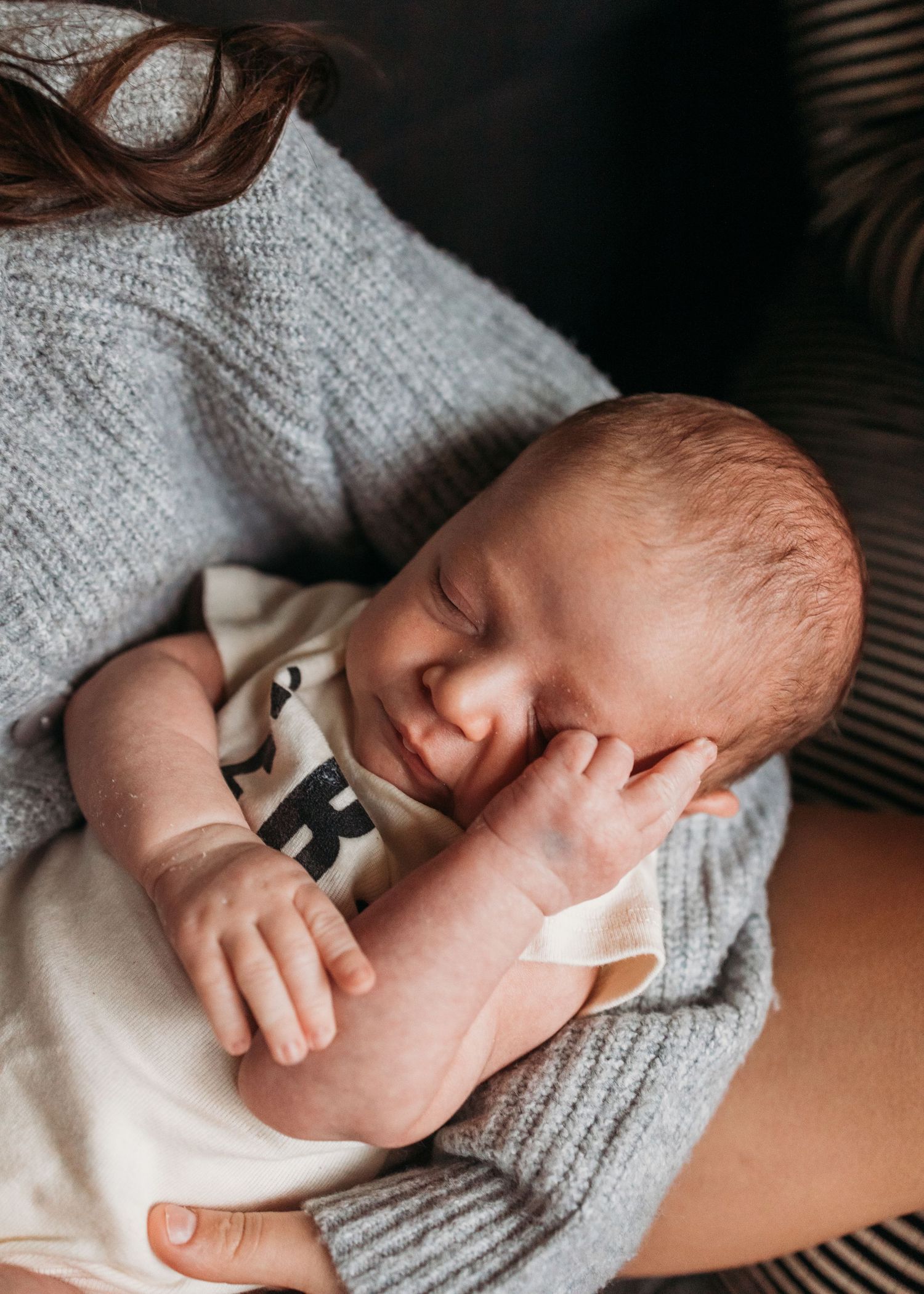 A tiny baby's hand grasps a finger while resting on a soft gray knitted blanket.