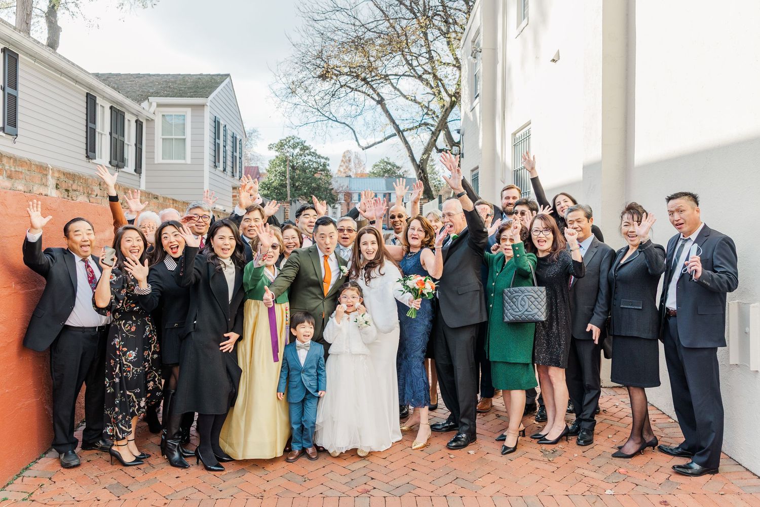 Large wedding party poses together outdoors in formal attire with bridesmaids in green dresses and groomsmen in suits.