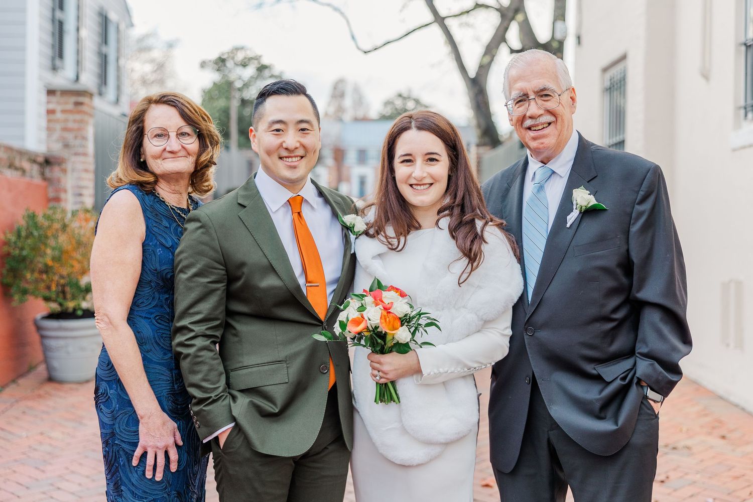 A small wedding party poses together outdoors wearing formal attire with the bride holding a peach and white bouquet.