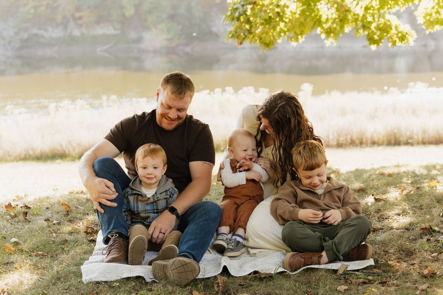 A family sits together on grass during a warm autumn day reading books in the park.
