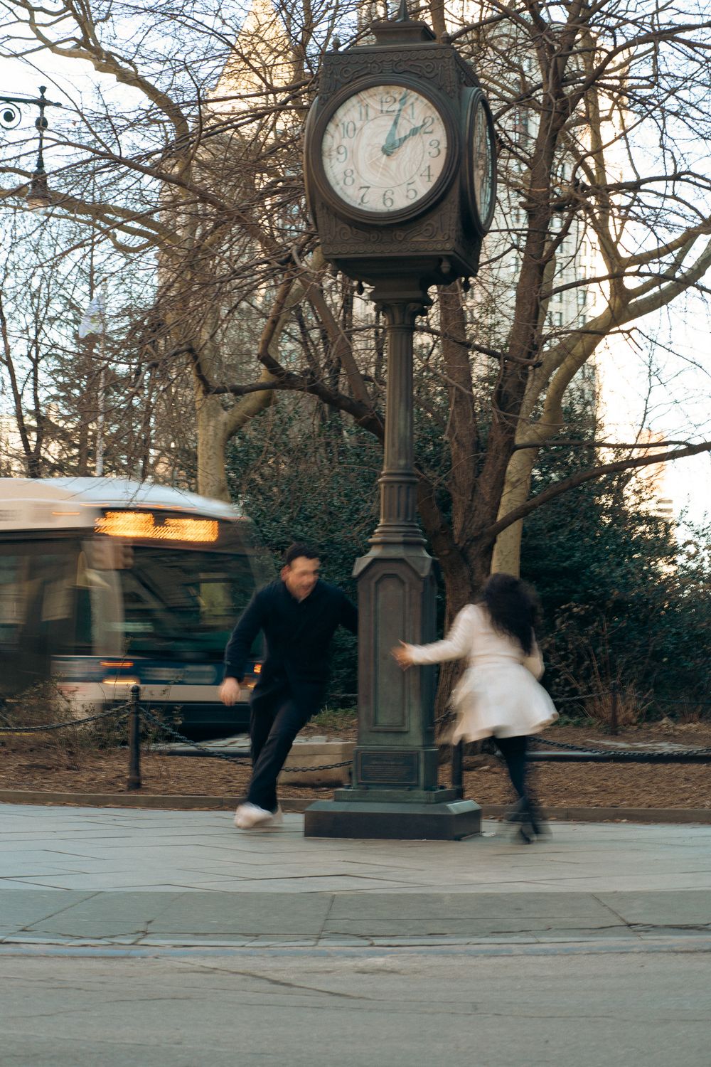 A sequence of motion blur photos showing a person spinning around a street clock in an urban park setting.