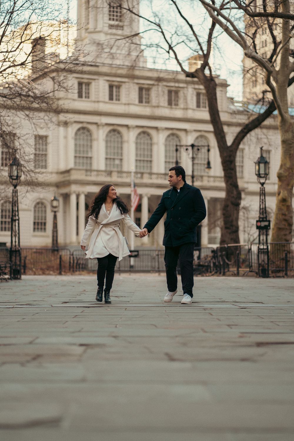 People running and playing in front of a historic building with classical architecture and bare winter trees.
