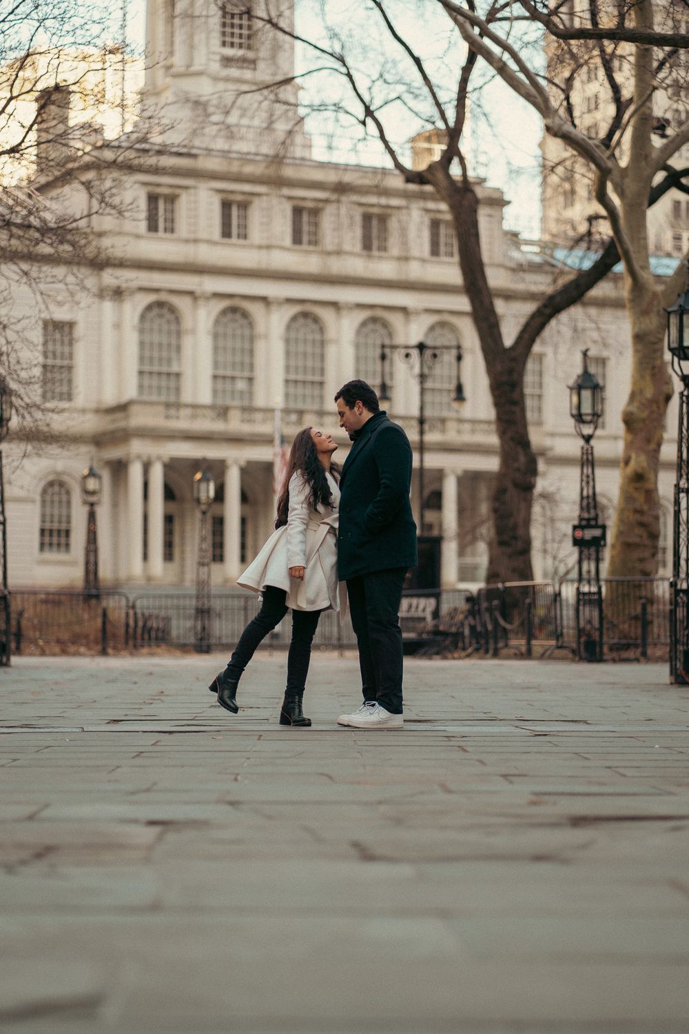 A romantic couple dancing together in front of a historic building with bare winter trees in the background.