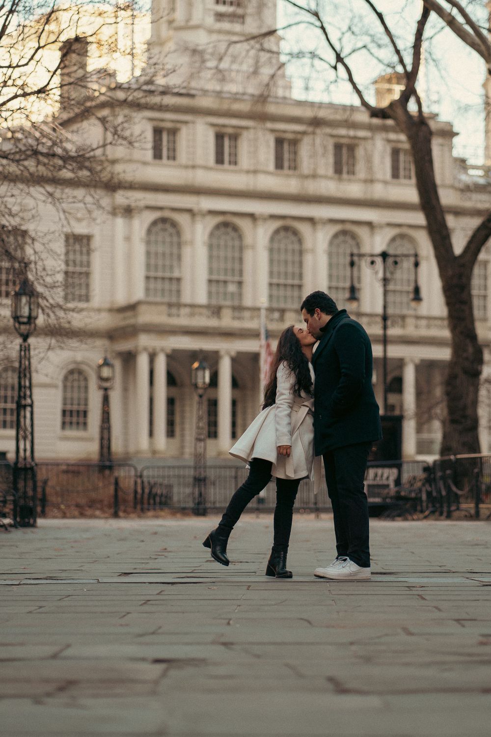 A couple shares a romantic moment in front of a historic stone building on a winter day in London.