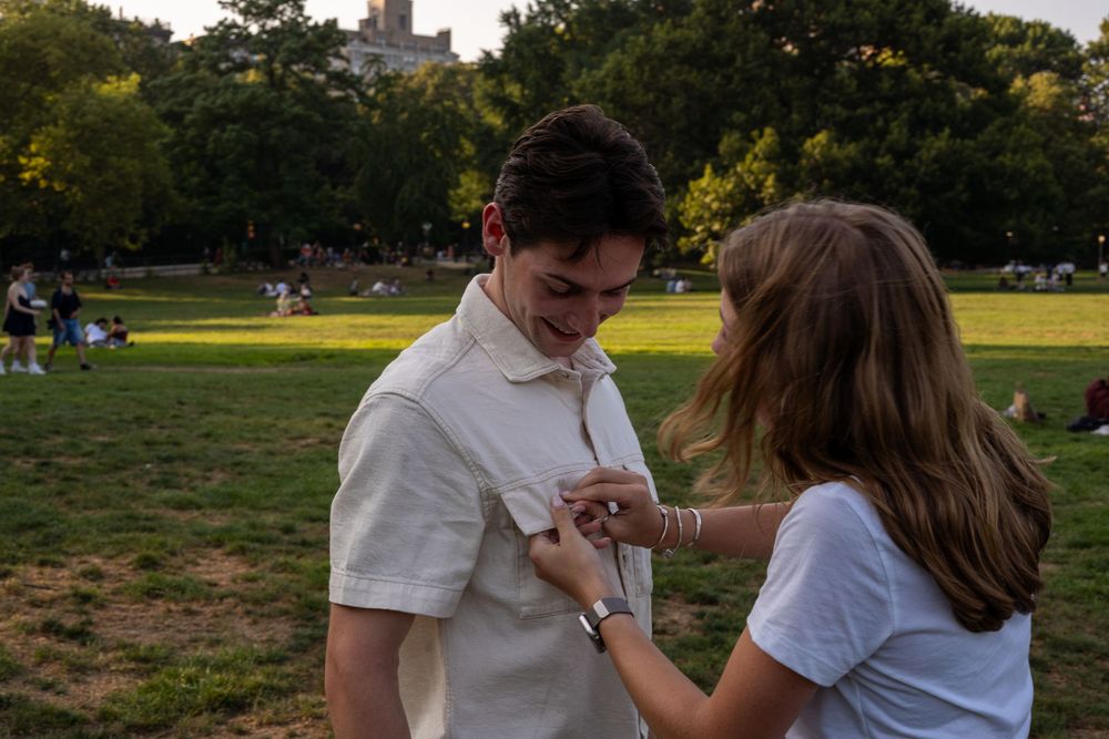 A couple shares a romantic moment at sunset in a grassy park setting.