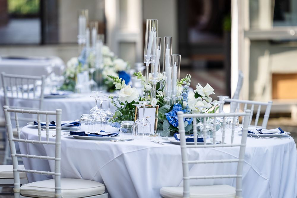 Elegant wedding reception table setting with blue and white flowers and silver chiavari chairs.