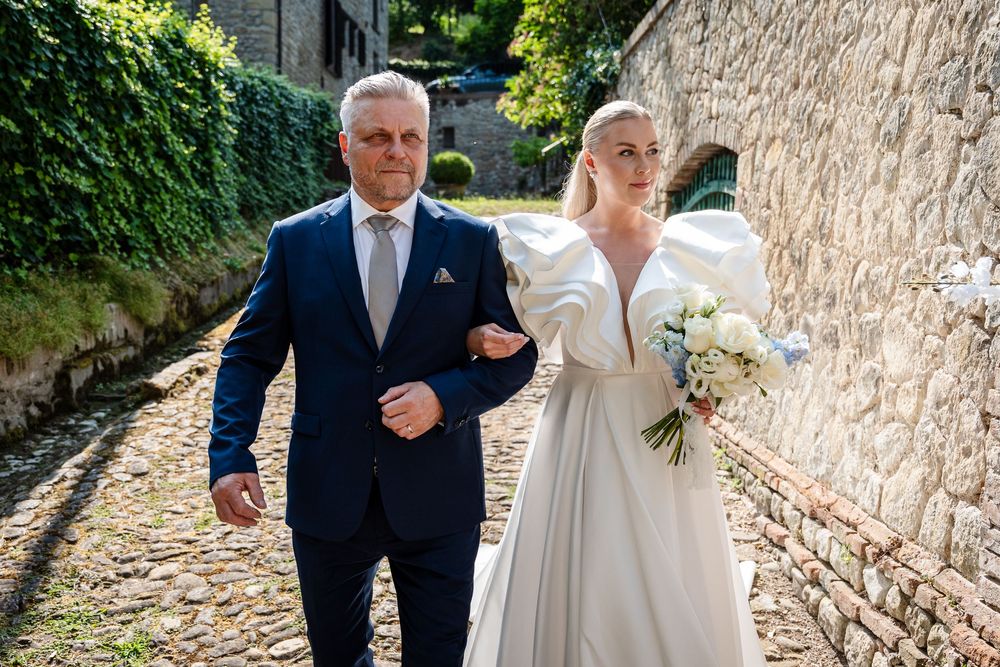 A couple walking arm in arm down a charming cobblestone path lined with ivy-covered walls.
