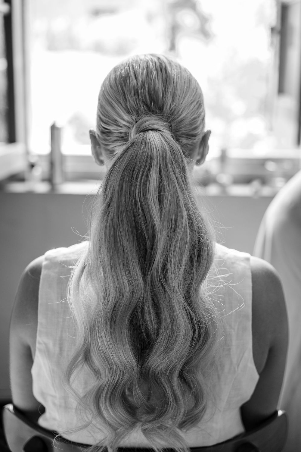 Elegant wavy bridal hairstyle shown from behind in a sleek ponytail style.