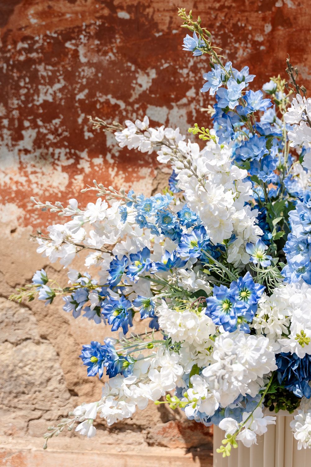 Beautiful blue and white floral arrangements displayed against a rustic terracotta wall background.