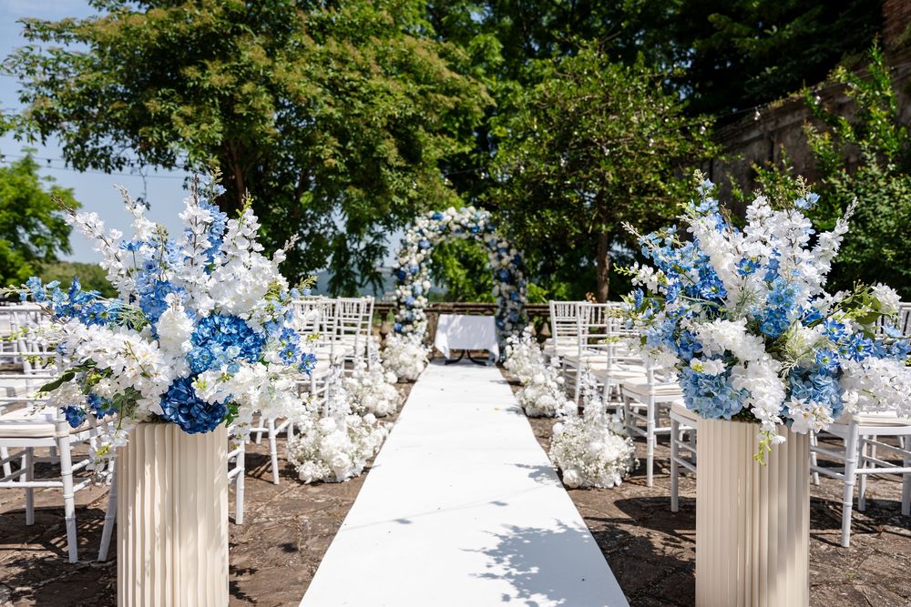 Elegant outdoor wedding ceremony setup with white chairs and floral arrangements under trees.