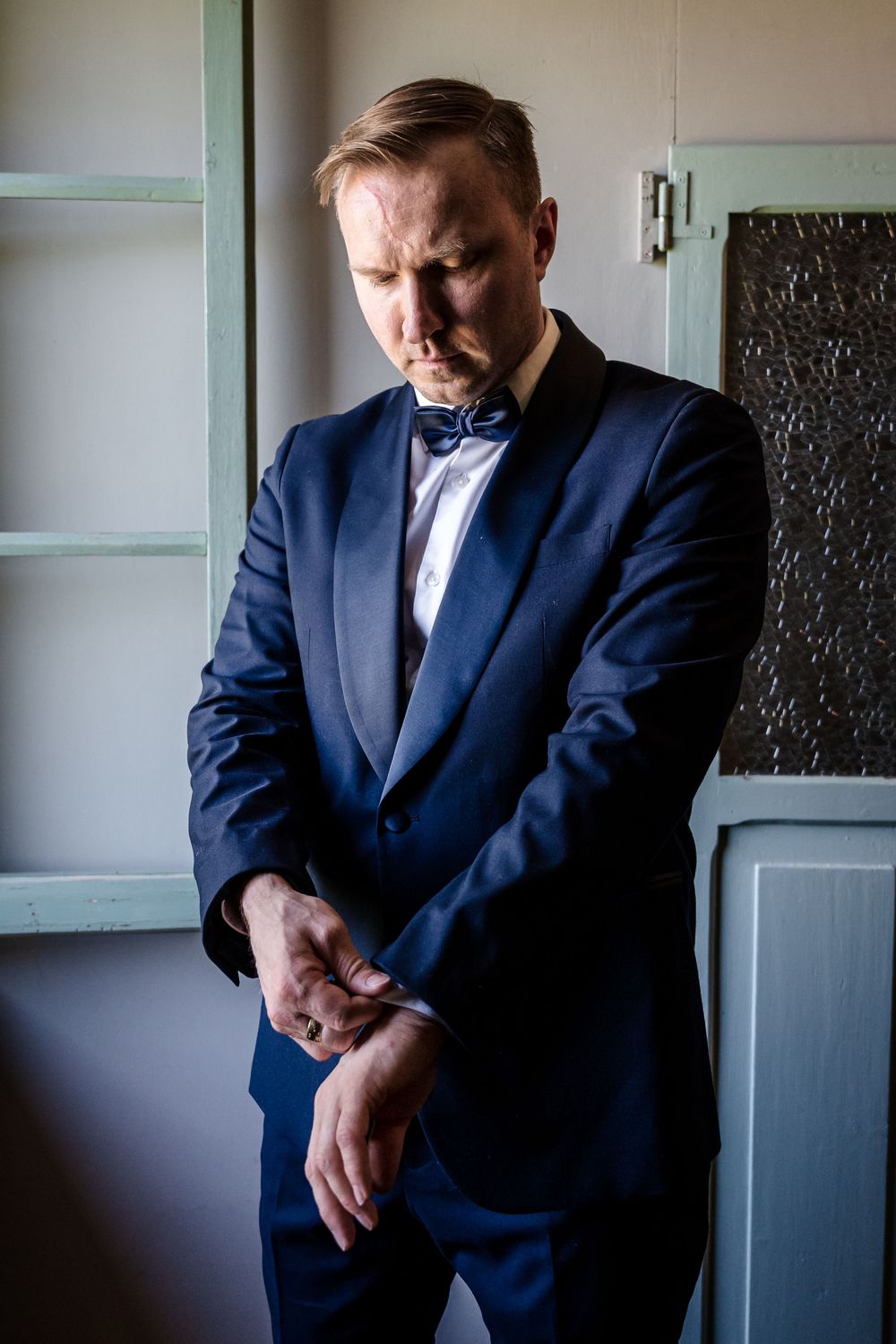 Groom in navy suit adjusts his cuffs while getting ready for the ceremony.