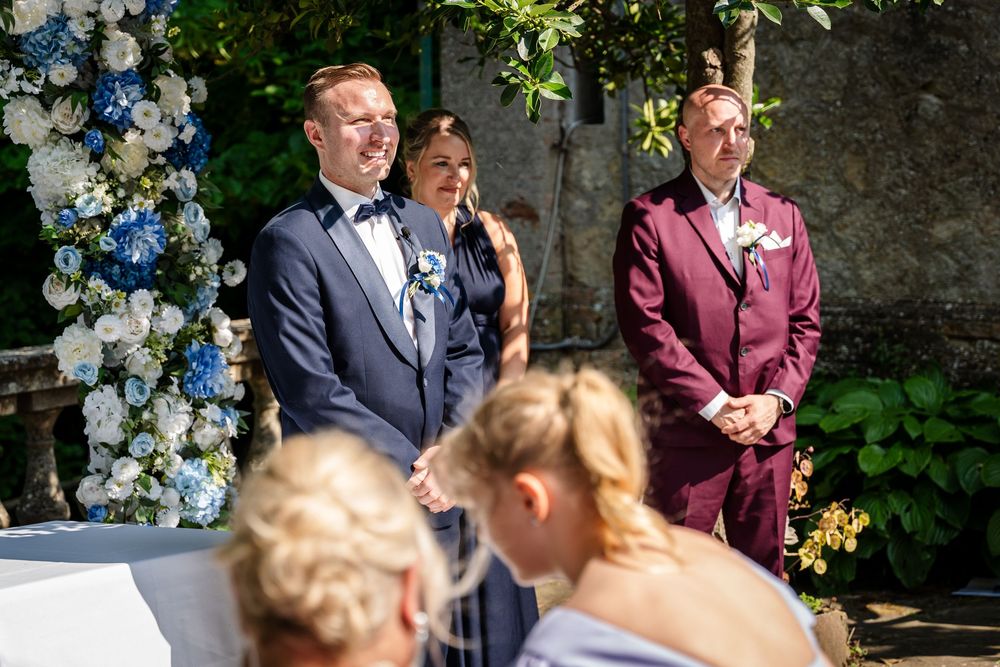 Wedding ceremony outdoors with blue floral arch and formal attire.