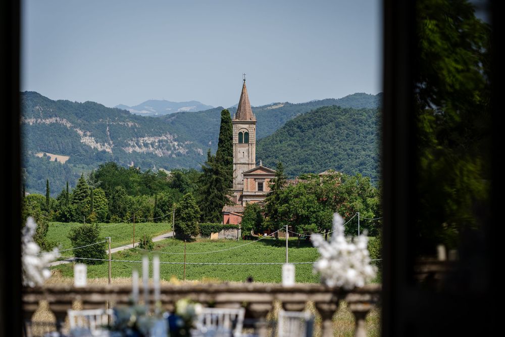 A picturesque church with bell tower nestled among green mountains under blue sky.