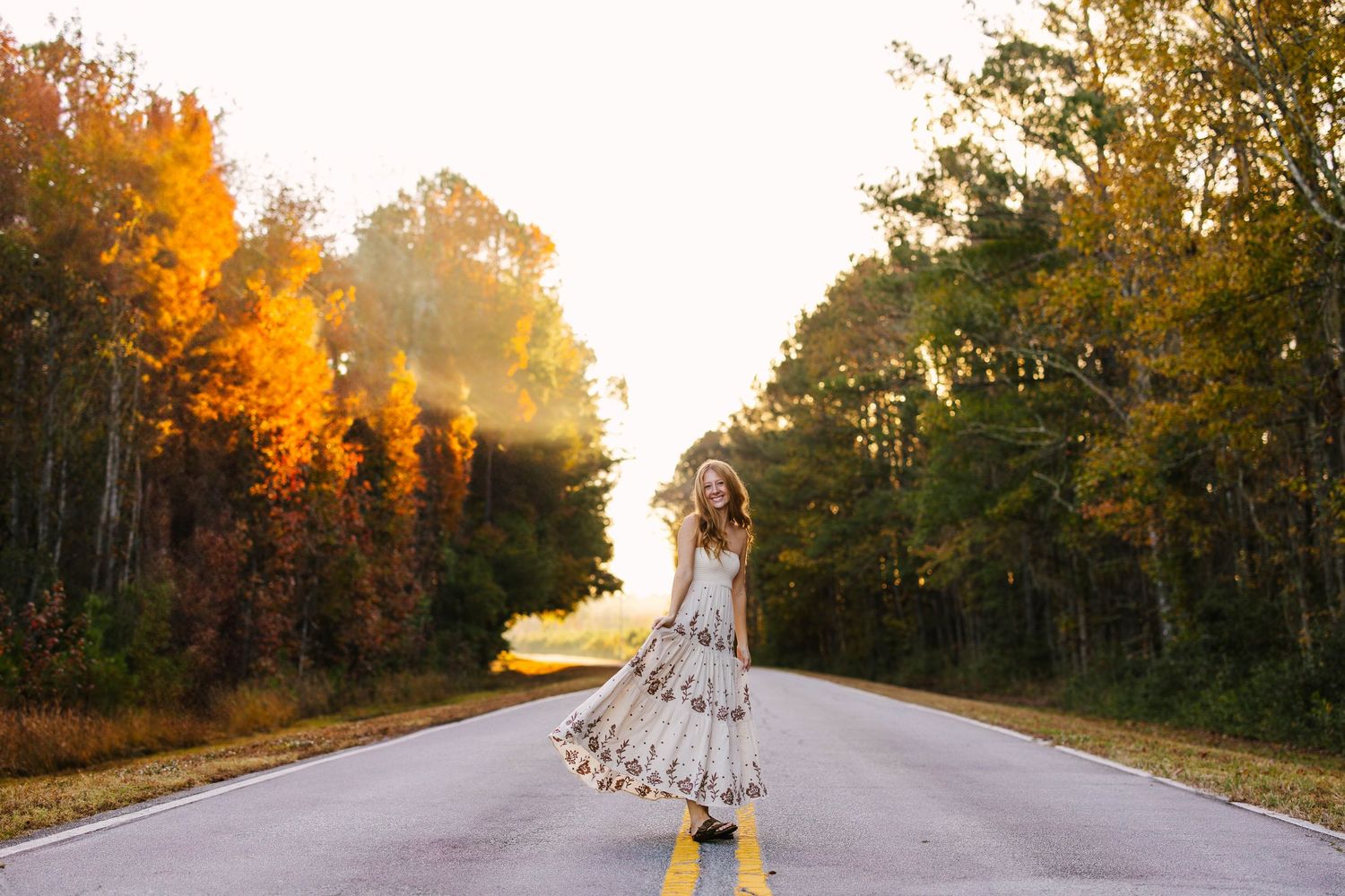 A winding country road curves through vibrant autumn trees with golden sunlight filtering through the foliage.