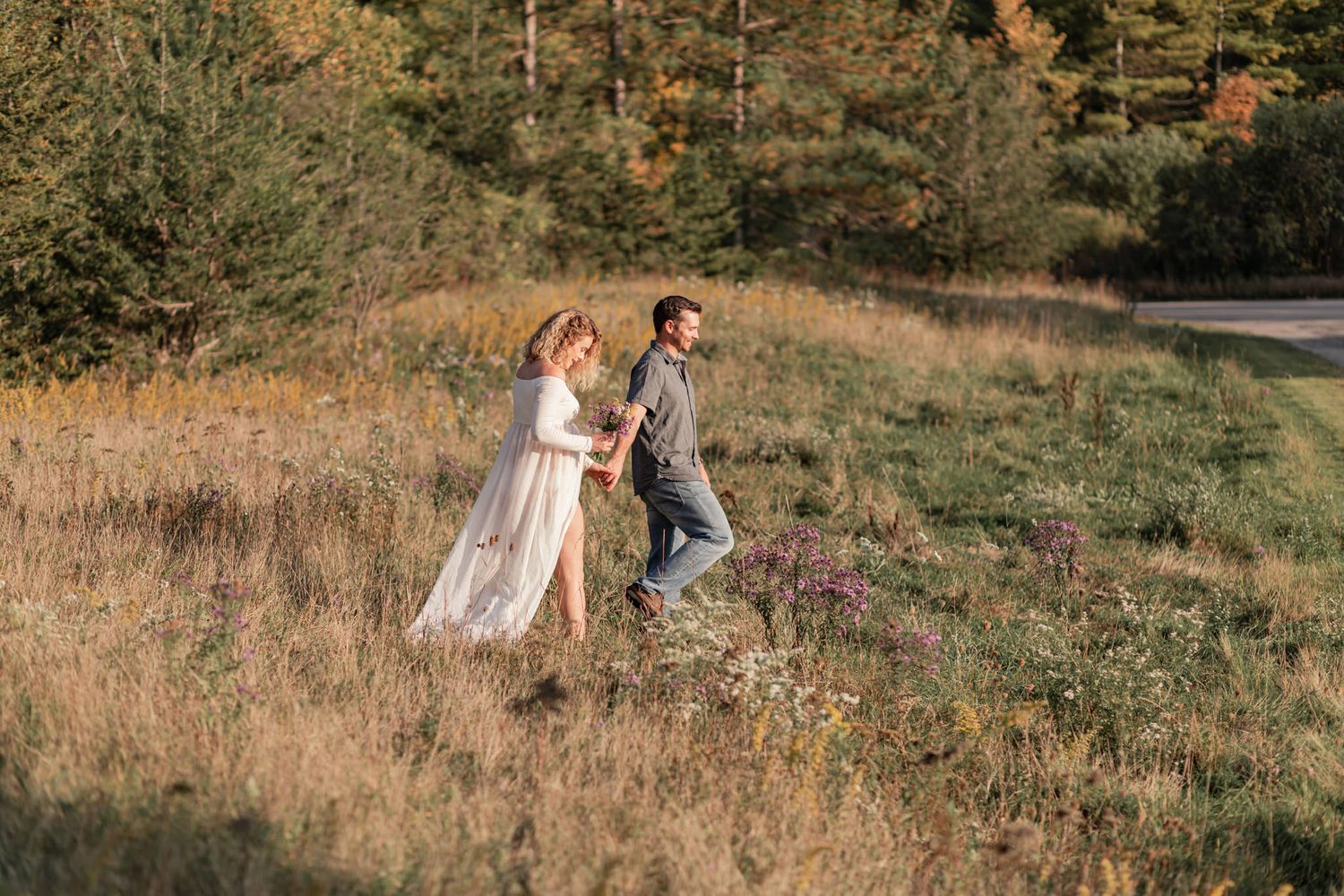 couple walk through wild flowers, hand in hand, at conservation area near kingston ontario sunset