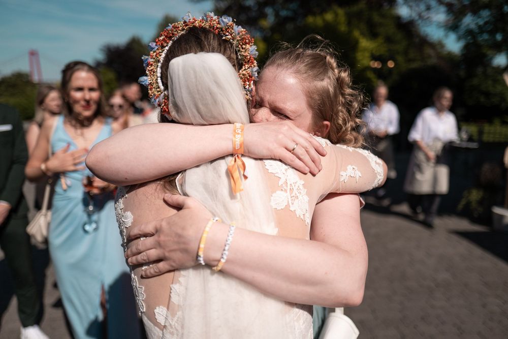 Herzliche Umarmung zwischen Braut und Brautjungfer nach der Trauung am Niederrhein. Natürliche Hochzeitsfotos voller Emotionen.