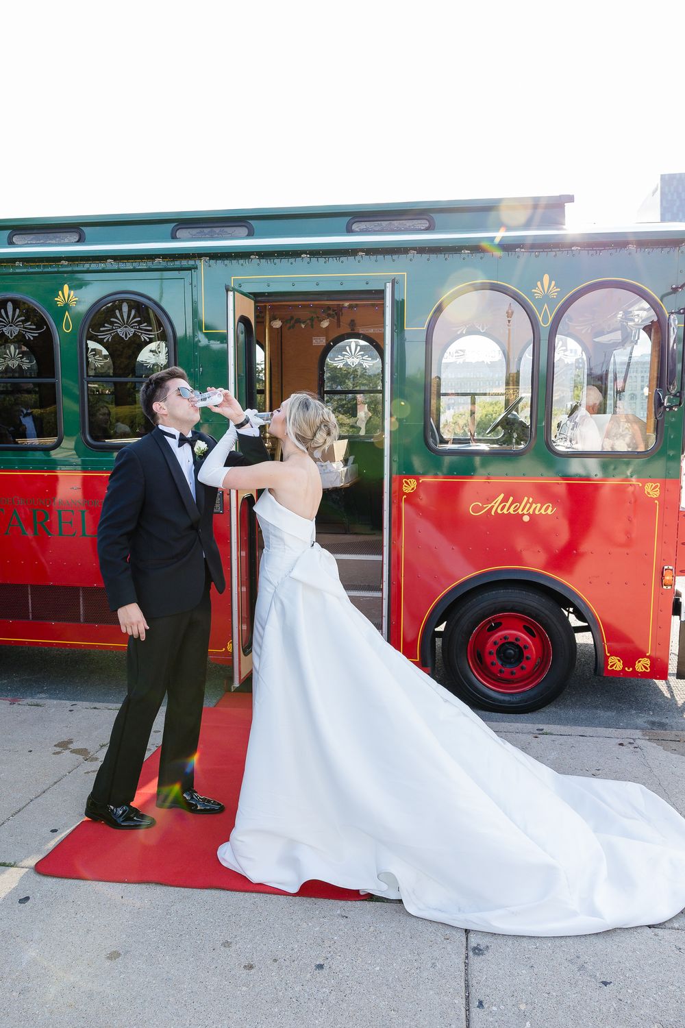 A couple poses for wedding photos in front of a vintage red trolley bus.