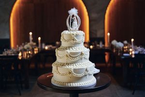 Elegant white wedding cake with pearl details and ornate piping displayed on dark table at reception.