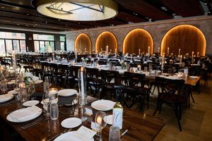 A modern restaurant interior with curved archways and warm lighting features elegant table settings and dark wood floors.
