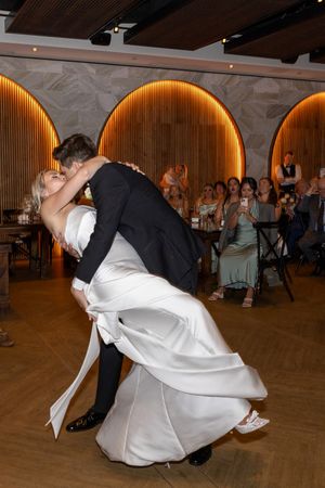 A couple performs a dramatic dance dip on a wooden dance floor at their wedding reception.