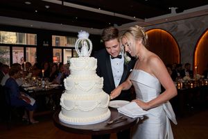 Wedding couple cutting their traditional white tiered cake together during evening reception celebration.