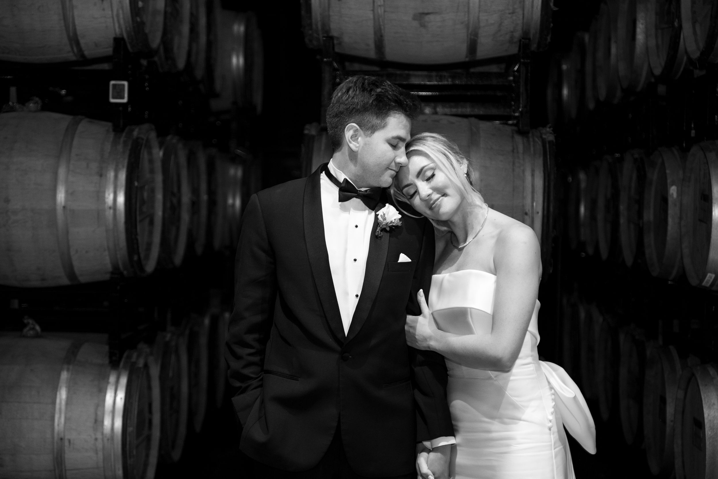 Romantic black and white portrait of couple sharing intimate moment in wine cellar.