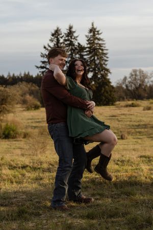 Joyful couple dancing in a golden field, woman in green dress and boots laughing as man in burgundy holds her close. taken by photographer